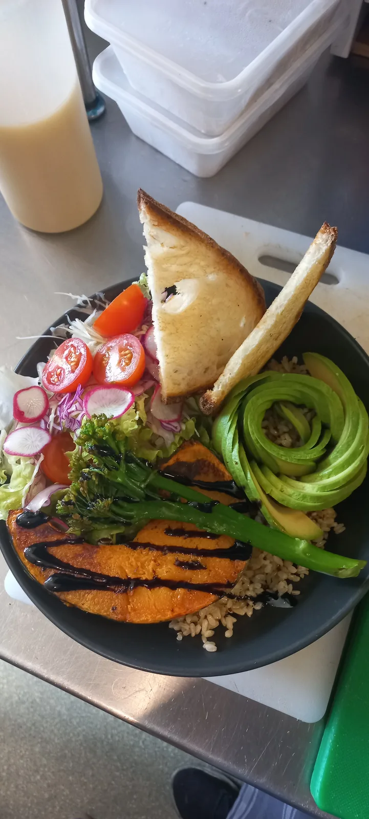 Original phone photo of a roast pumpkin, broccolini and avocado grain bowl on a stainless steel bench.